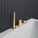 Wannenrandarmatur in Brushed Gold von Ideal Standard, bestehend aus einem Stand- und einem Umstellventil, montiert auf einem weißen Wannenrand vor einer schwarzen Fliesenwand.